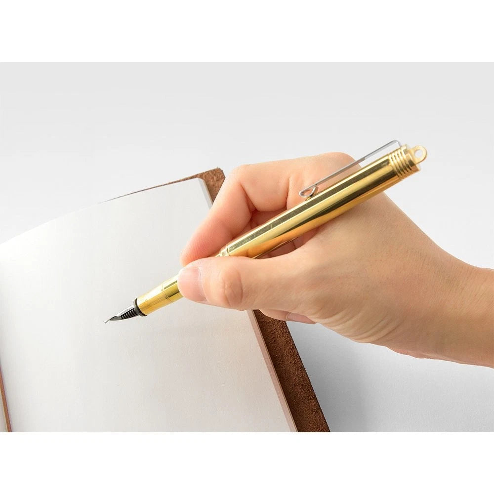 Midori Compact Brass Fountain Pen in gold, fine nib, shown in use while writing on paper.