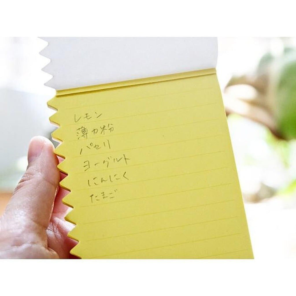 Orissi notepad with yellow lined pages, held in hand and containing handwritten Japanese list.