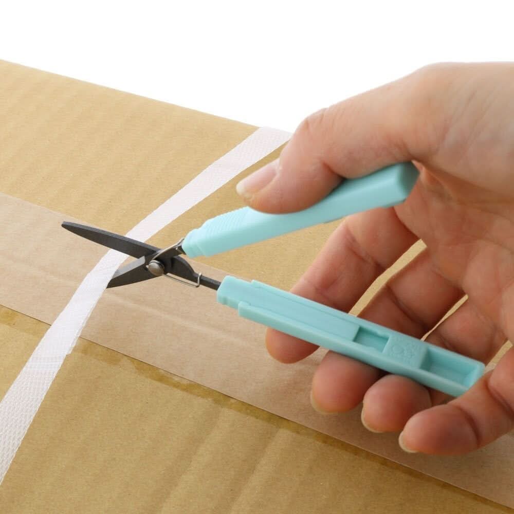 Sun-Star Akeruno Stickyle turquoise scissors in use, cutting through white strapping on a cardboard box.
