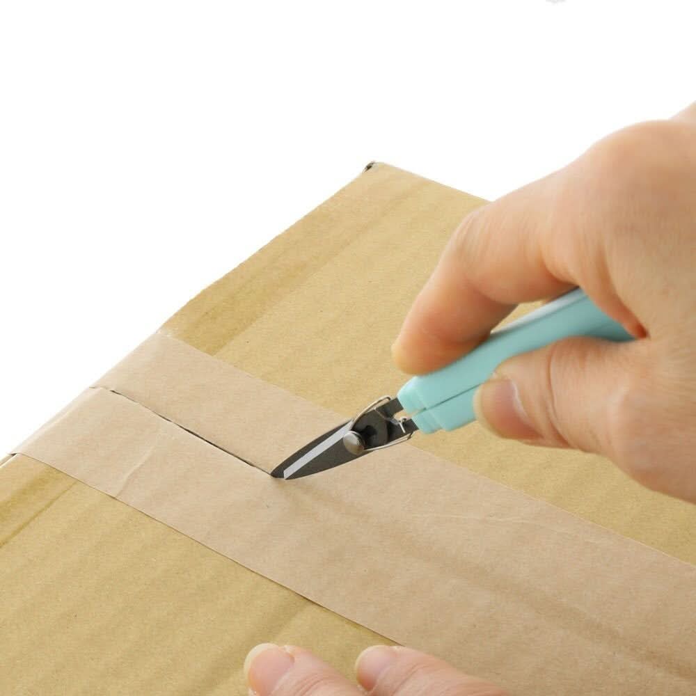 Sun-Star Akeruno Stickyle scissors and box cutter in turquoise, used to cut sealing tape on a cardboard box.