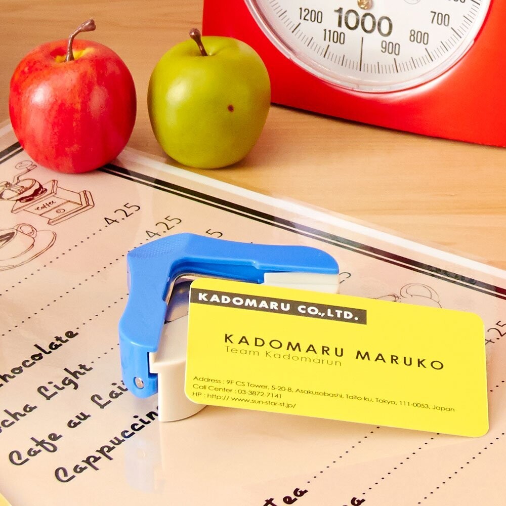 Sun-Star KadoMaru 3 Corner Cutter in blue being used to round the edge of a yellow business card on a desk.