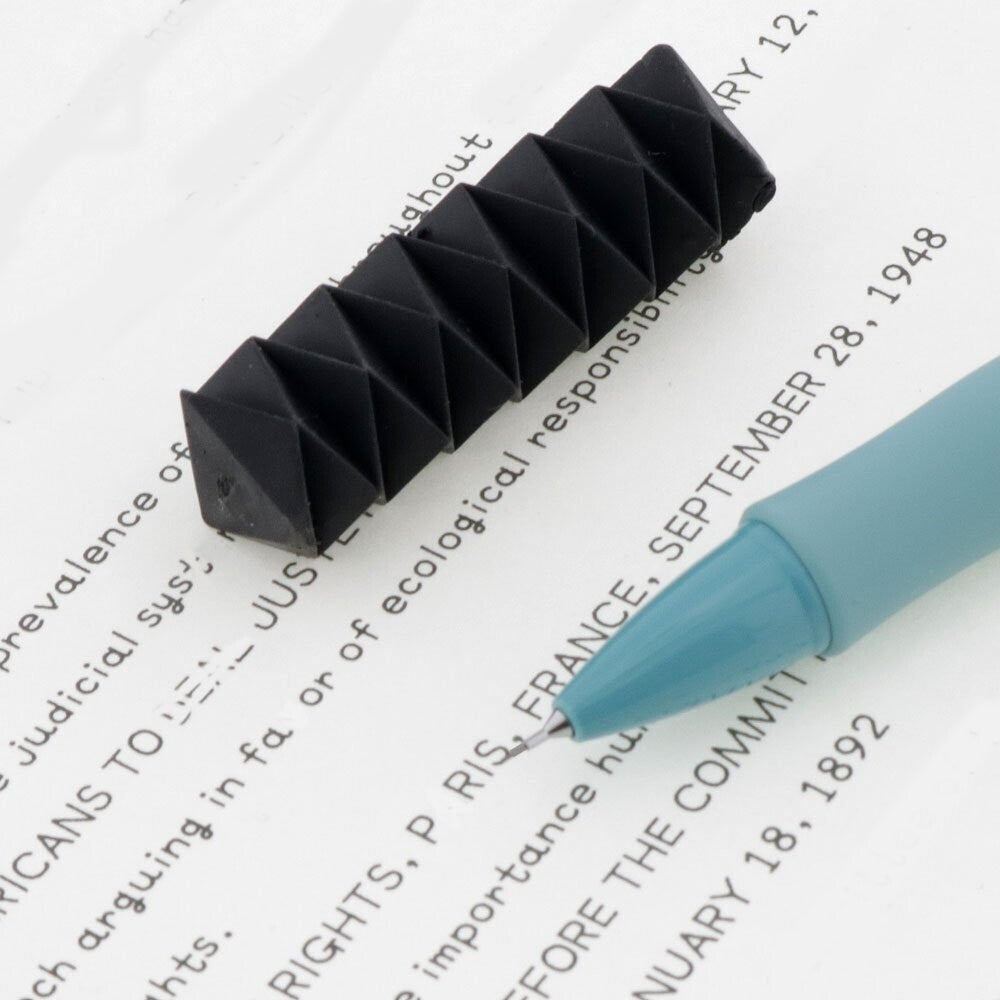 Black Sun-Star Zig Zag Multi-Angle Eraser on paper erasing printed text next to a blue mechanical pencil.