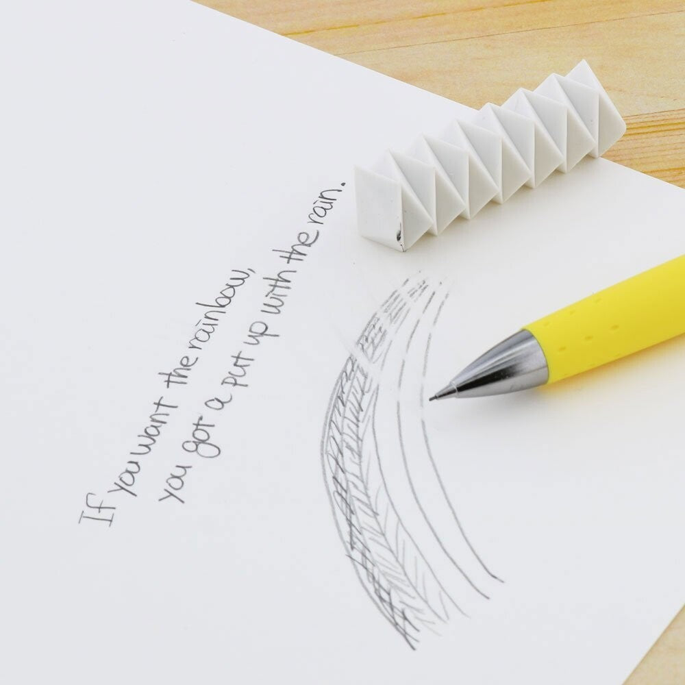 White Sun-Star Zig Zag Multi-Angle Eraser on paper erasing pencil marks next to a yellow mechanical pencil.