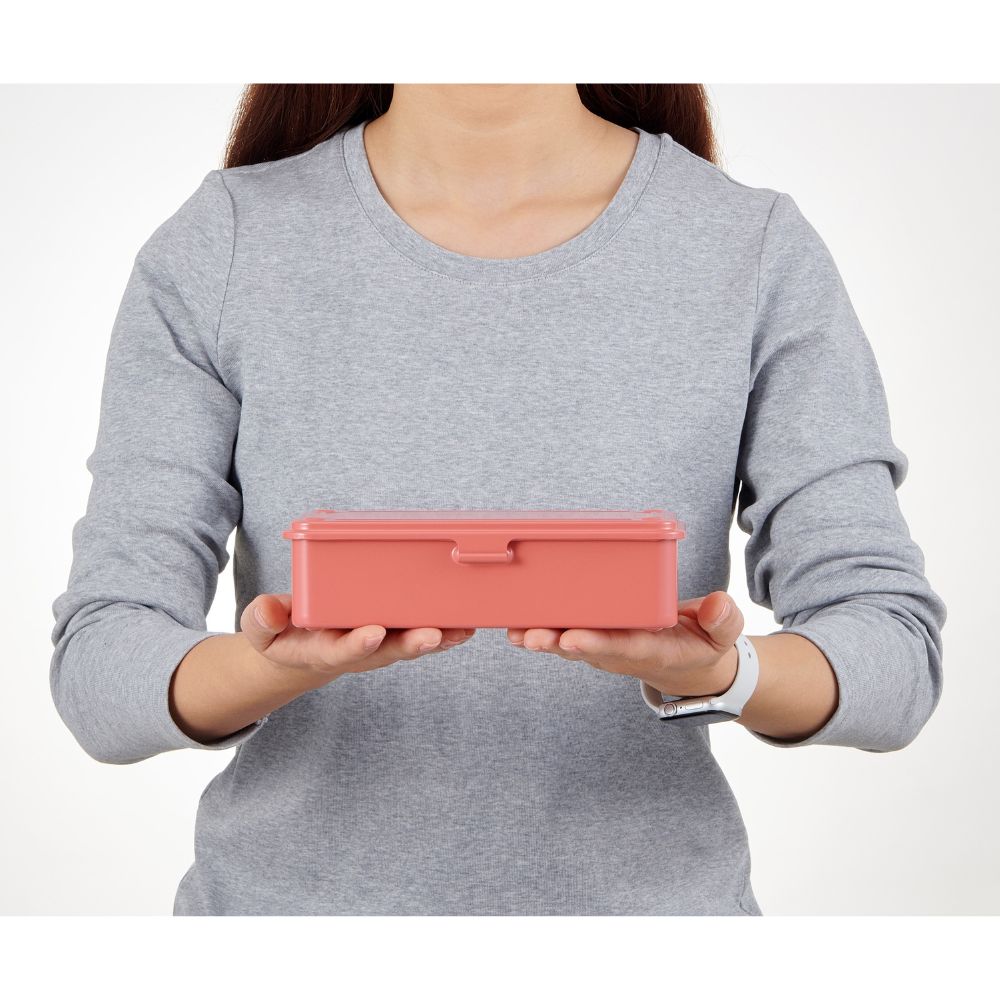 Person holding a coral TOYO STEEL T-190 toolbox with both hands, illustrating its compact size.