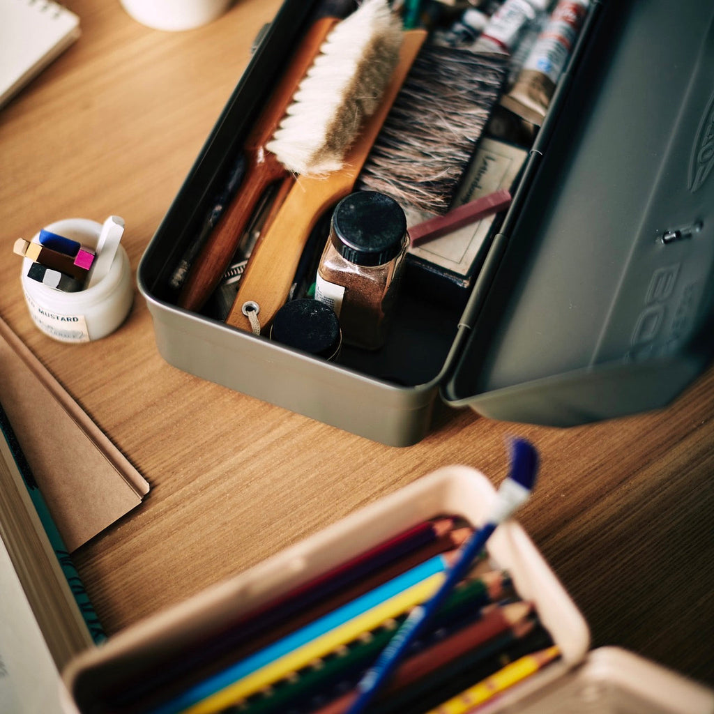 Close-up of an open TOYO Y-350 toolbox in khaki, filled with art supplies such as brushes, jars, and pencils on a wooden desk.