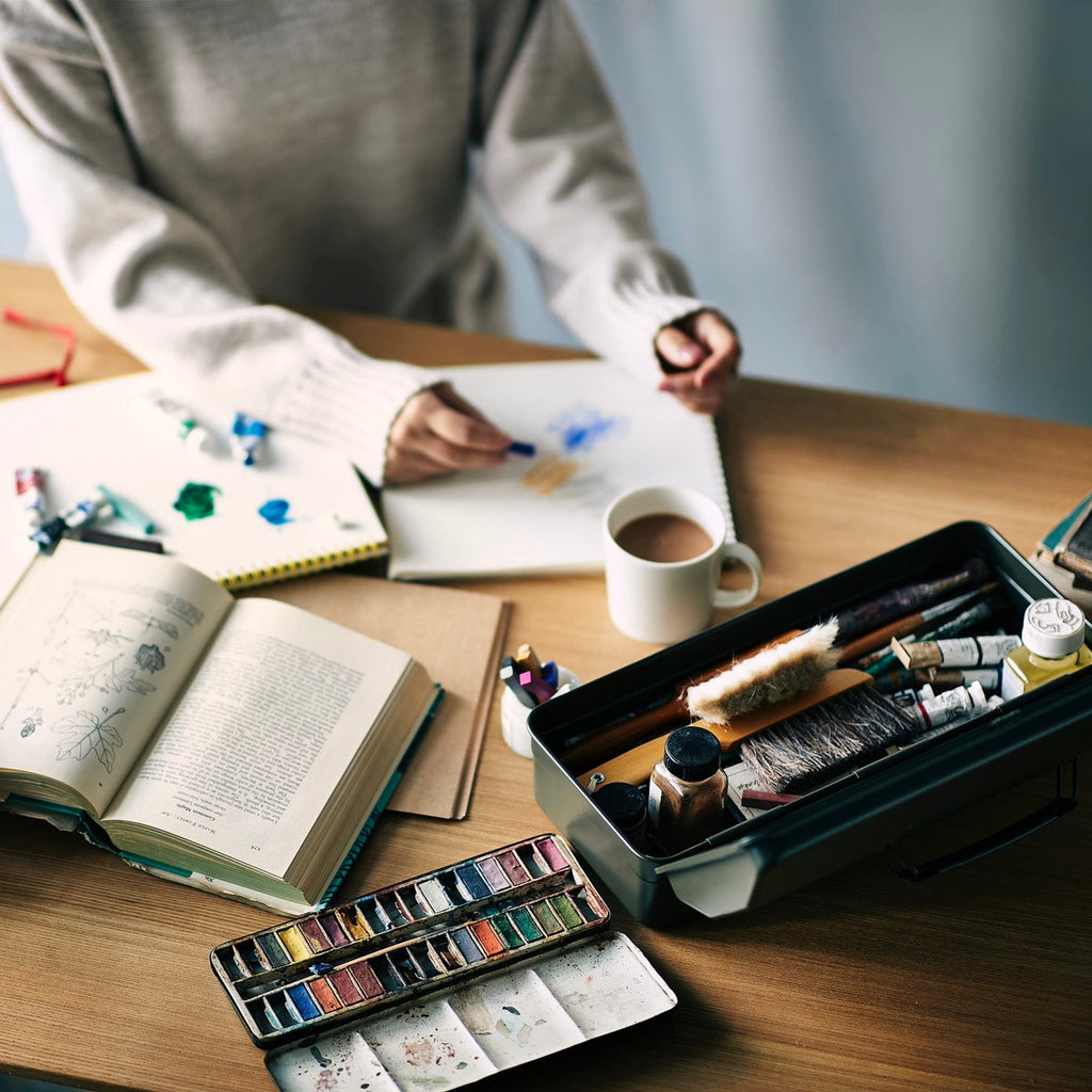TOYO Y-350 toolbox on a creative workspace table, open and holding art tools, while a person sketches with watercolours.