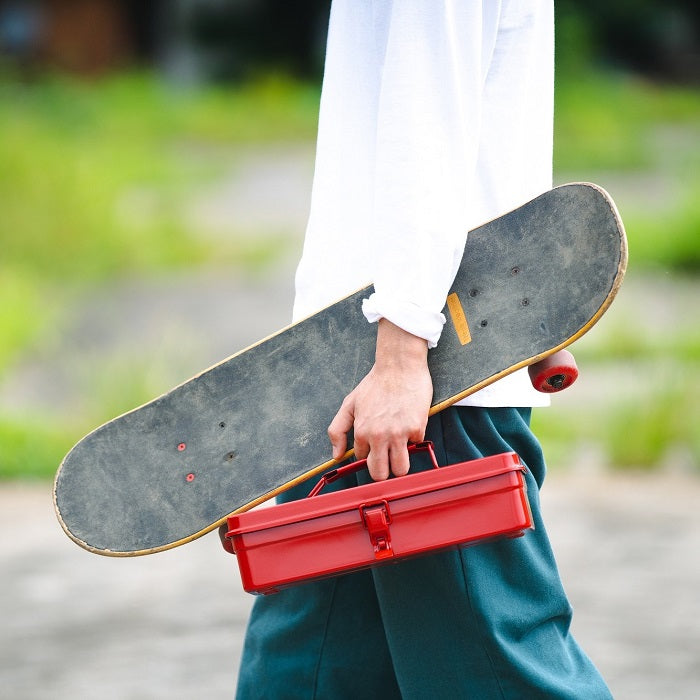 Person holding a red TOYO T-320 toolbox alongside a skateboard, outdoors.